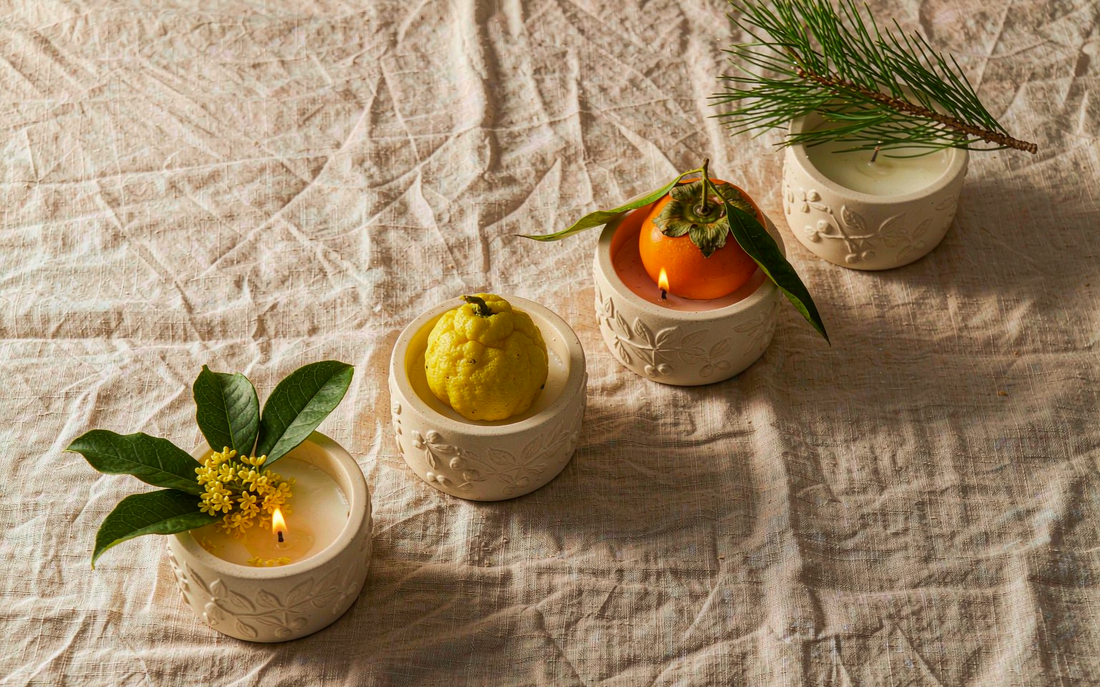 Four fall candles styled with osmanthus, yuzu, persimmon and pine sprigs