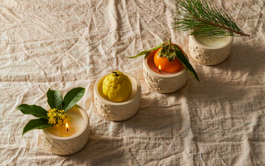 Four fall candles styled with osmanthus, yuzu, persimmon and pine sprigs
