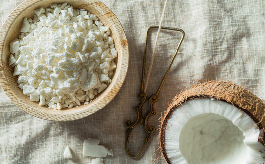 Soy wax flakes in a wooden bowl beside a fresh coconut - a coconut-soy wax blend